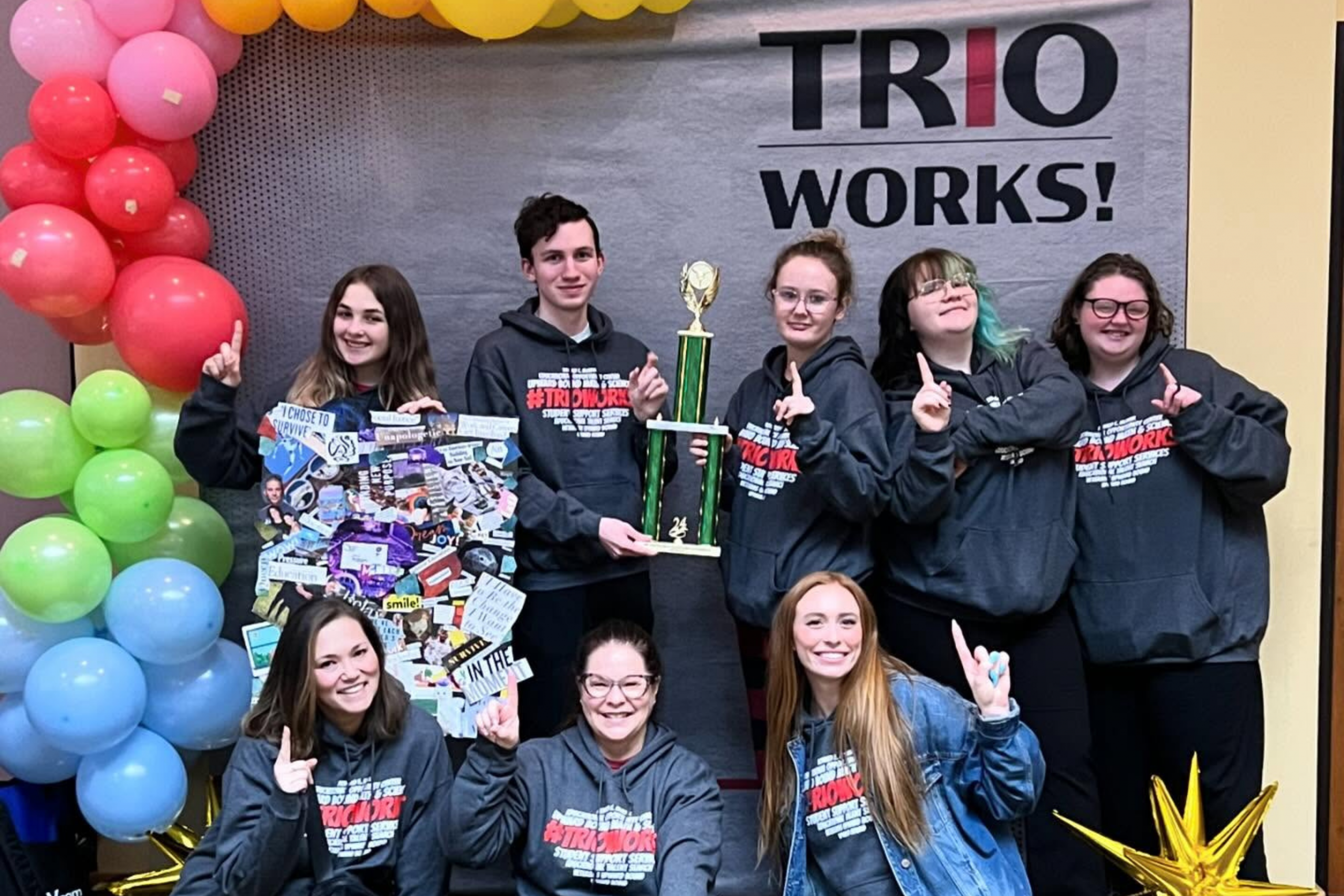 Upward Bound students and staff standing in front of a TRIO back drop holding a trophy